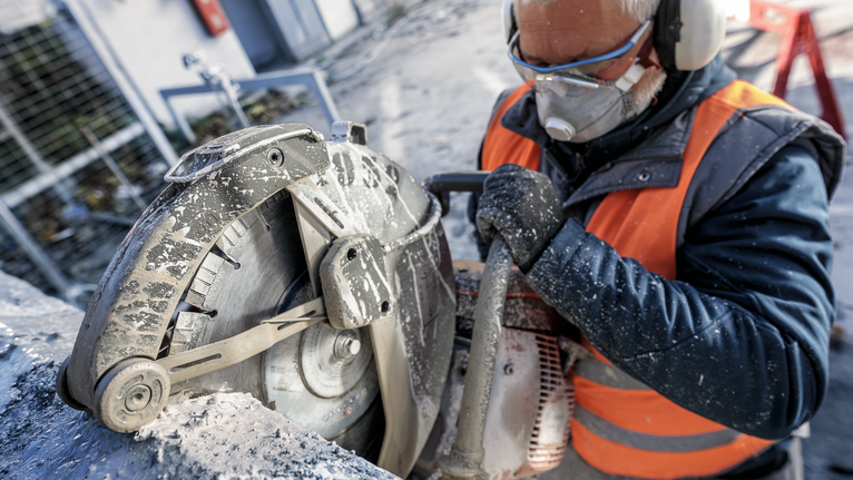 Eine Person mit Sicherheitsausrüstung schneidet Beton mit einer Kreissäge.