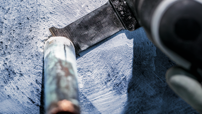 Eine Person mit Sicherheitsausrüstung schneidet mit einer Säbelsäge durch ein Metallrohr.