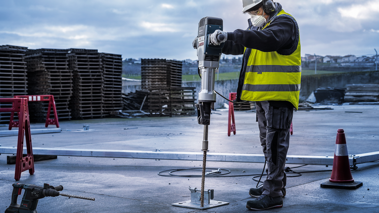 Eine Person mit Sicherheitsausrüstung bohrt auf einer Baustelle in Beton.