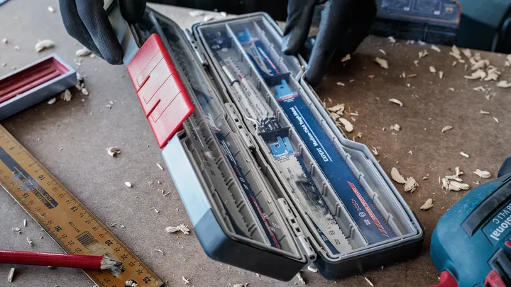 Eine Person mit Sicherheitsausrüstung öffnet einen Koffer mit Sägeblättern auf einer Werkbank.