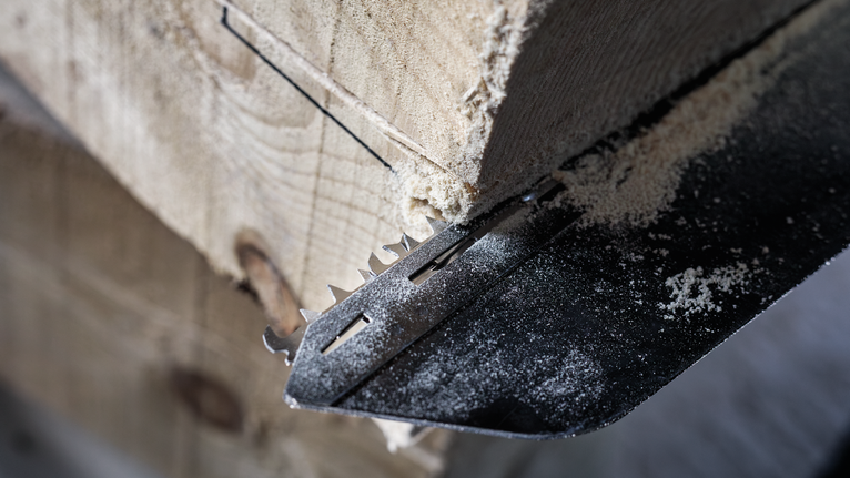 Sägeblatt schneidet durch einen dicken Holzbalken, Sägemehl ist sichtbar.
