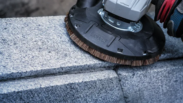 Eine Person mit Sicherheitsausrüstung poliert eine Betonoberfläche mit einem Elektrowerkzeug.