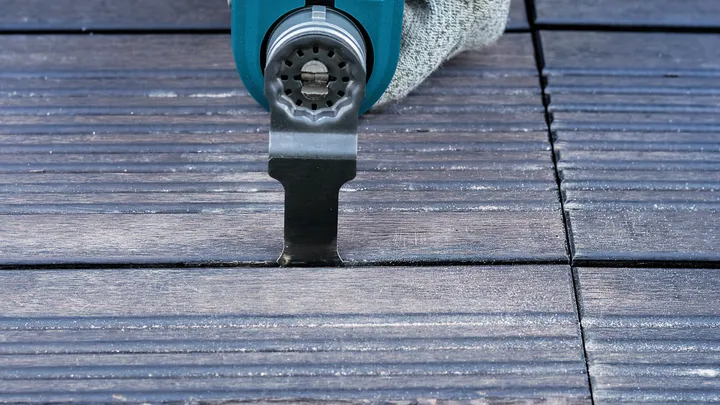 Eine Person, die Schutzausrüstung trägt, benutzt ein Multifunktionswerkzeug zum Schneiden von Holzterrassendielen.