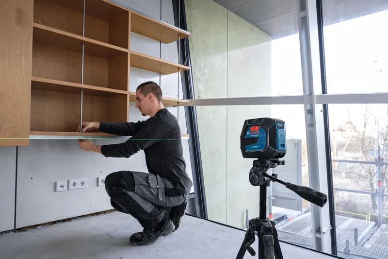 Eine Person installiert ein Regal und verwendet dabei ein Lasernivelliergerät, um die Ausrichtung sicherzustellen.