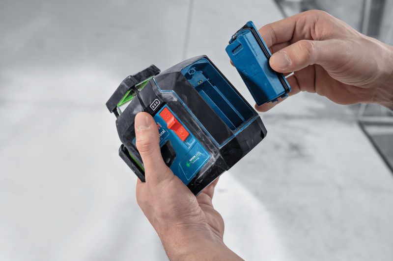 Eine Person setzt auf einer Baustelle eine Batterie in ein Lasernivelliergerät ein.