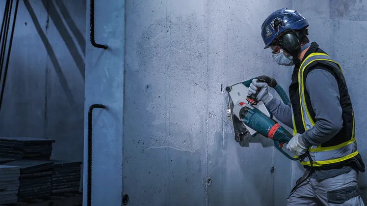 Eine Person mit Sicherheitsausrüstung schneidet mit einem Elektrowerkzeug eine Betonwand.