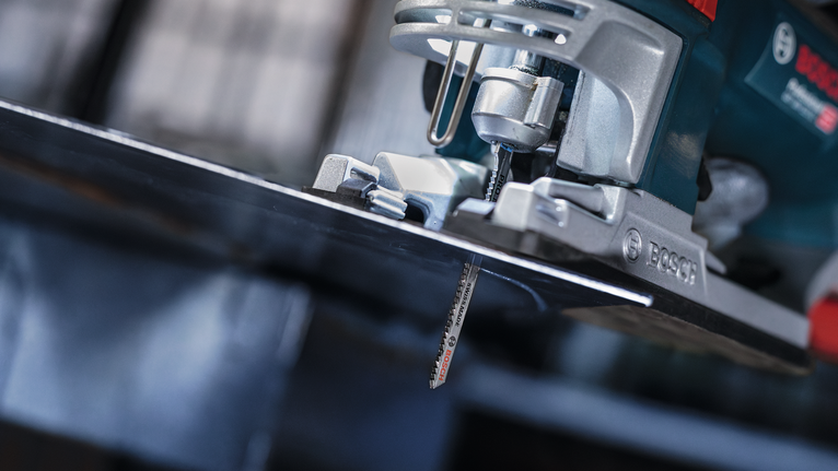 Eine Stichsäge schneidet in einer Werkstatt durch ein Metallblech.