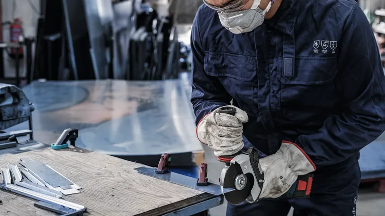 Eine Person mit Sicherheitsausrüstung schneidet mit einer Schleifmaschine Metallbleche.