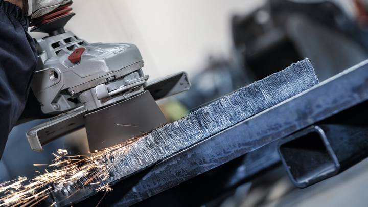 Eine Person mit Schutzausrüstung schleift eine Metallkante und erzeugt dabei Funken.