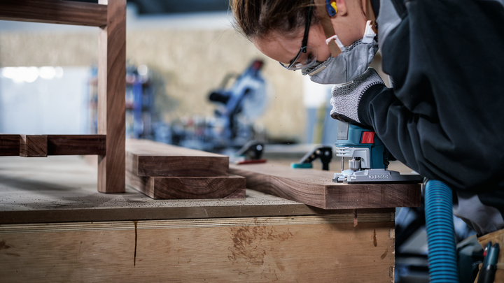 Eine Person mit Sicherheitsausrüstung schleift Holzmöbel mit einem Elektrowerkzeug.