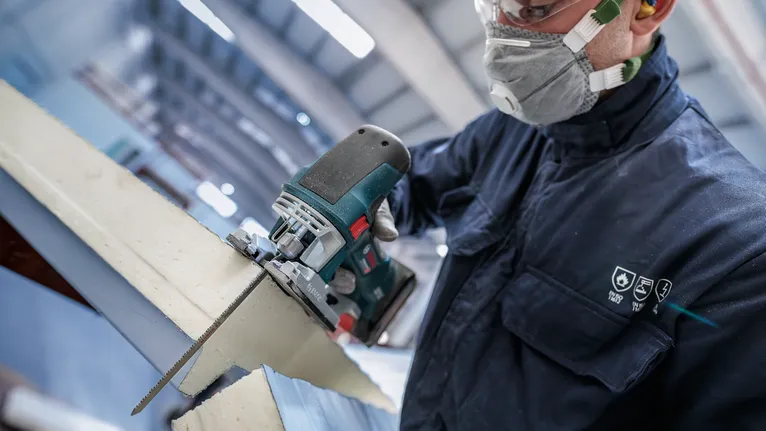 Eine Person mit Sicherheitsausrüstung schneidet Schaumstoffisolierung mit einer elektrischen Stichsäge.