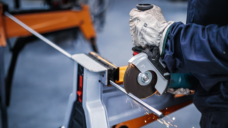 Person mit Sicherheitsausrüstung, die mit einem Elektrowerkzeug eine Metallstange schneidet.