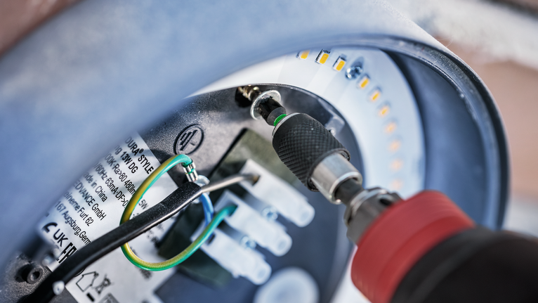 Akkuschrauber zieht eine Schraube in einer runden LED-Leuchte fest.