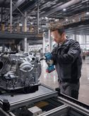 Eine Person mit Sicherheitsausrüstung verwendet einen Akku-Schlagschrauber an einer Motorbaugruppe.
