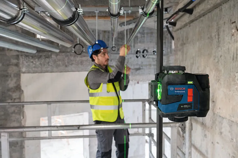 Eine Person mit Sicherheitsausrüstung richtet Rohre mit einem Lasernivelliergerät aus.