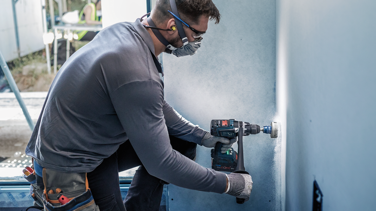 Eine Person mit Sicherheitsausrüstung bohrt mit einem Elektrowerkzeug ein Loch in eine Wand.