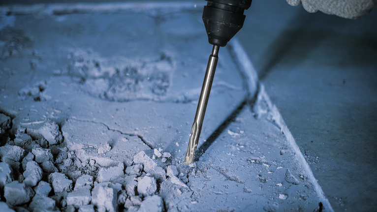 Eine Person mit Sicherheitsausrüstung verwendet einen Abbruchbohrer, um Beton aufzubrechen.