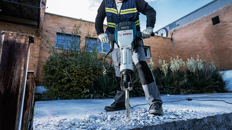 Eine Person mit Sicherheitsausrüstung bricht im Freien mit einem Abbruchhammer Beton auf.