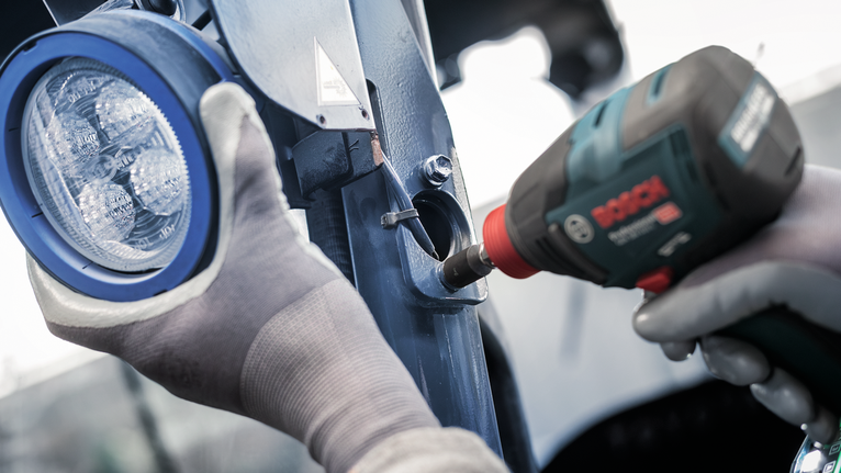 Eine Person mit Sicherheitsausrüstung verwendet ein Elektrowerkzeug, um eine Leuchte auf Metall zu installieren.