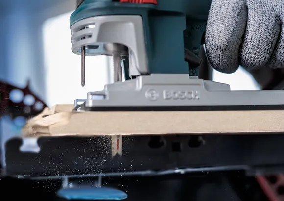 Person mit Sicherheitsausrüstung schneidet Holz mit einer Stichsäge.