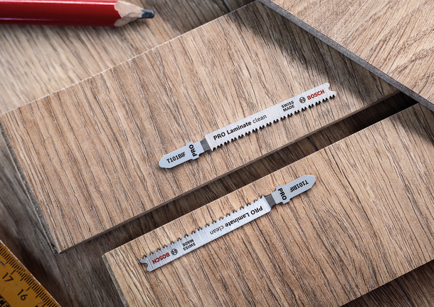 Zwei Stichsägeblätter auf Laminatholzplatten, daneben ein Bleistift und ein Lineal.