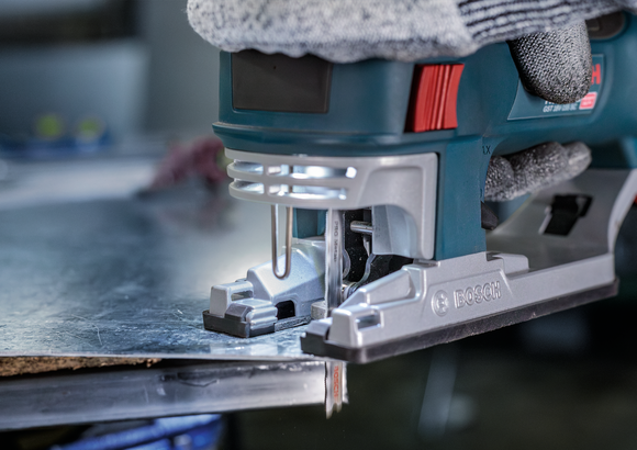 Eine Person mit Sicherheitsausrüstung schneidet mit einer Stichsäge ein Metallblech.