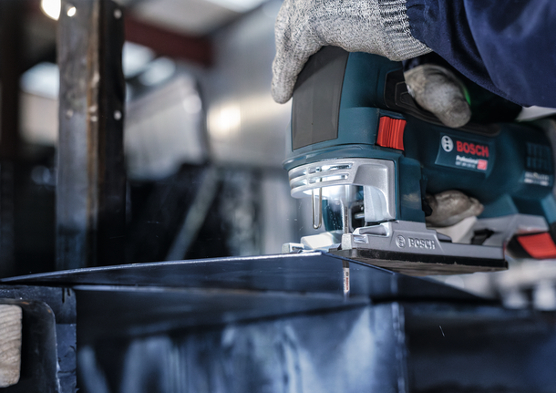 Eine Person mit Sicherheitsausrüstung schneidet in einer Industrieumgebung Metall mit einer Stichsäge.