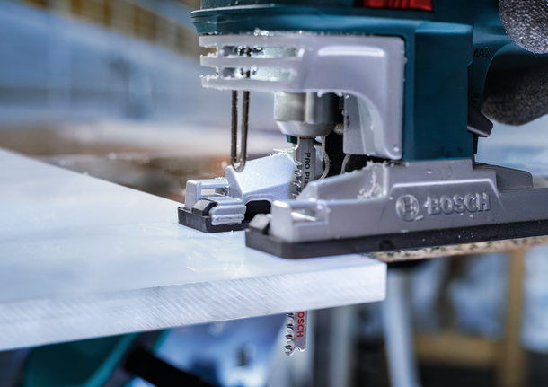 Stichsäge schneidet durch eine weiße Tafel in einer Werkstatt.