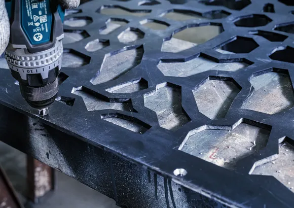Eine Person mit Sicherheitsausrüstung verwendet einen Bohrer auf einem gemusterten Metallblech.
