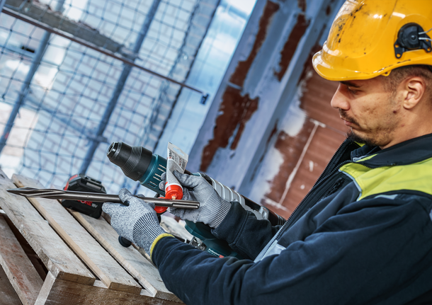 Eine Person mit Sicherheitsausrüstung trägt auf einer Baustelle Schmiermittel auf einen Bohraufsatz auf.