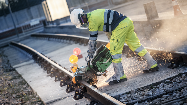 Eine Person mit Sicherheitsausrüstung schneidet mit einer Hochleistungssäge ein Eisenbahngleis.