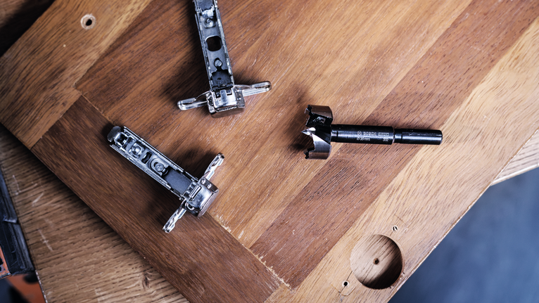 Bohrer und Schrankscharniere werden auf einem Holzbrett mit vorgebohrten Löchern platziert.