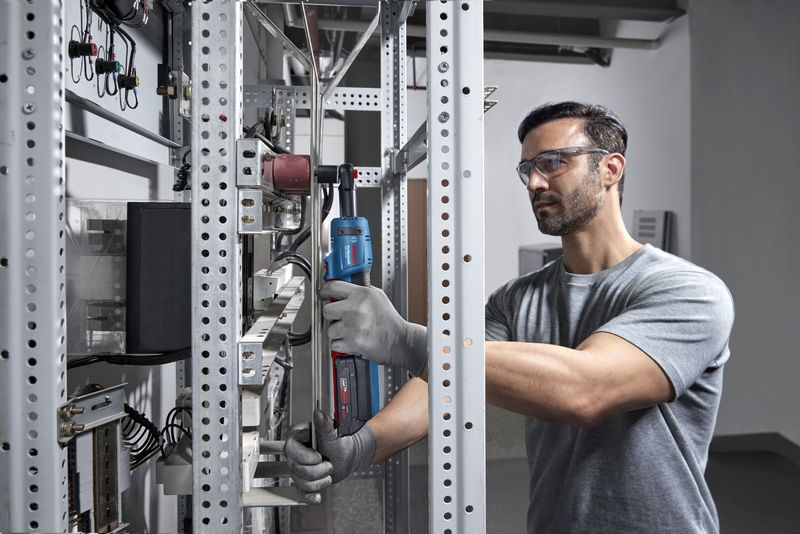 Eine Person mit Sicherheitsausrüstung verwendet einen Akku-Ratschenschlüssel an einem Metallgestell.