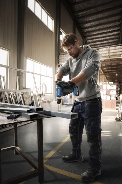 Eine Person mit Schutzausrüstung bohrt in einer Werkstatt in einen Metallträger.