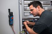 Eine Person überprüft elektrische Leitungen in einem Bedienfeld mit einem digitalen Multimeter.