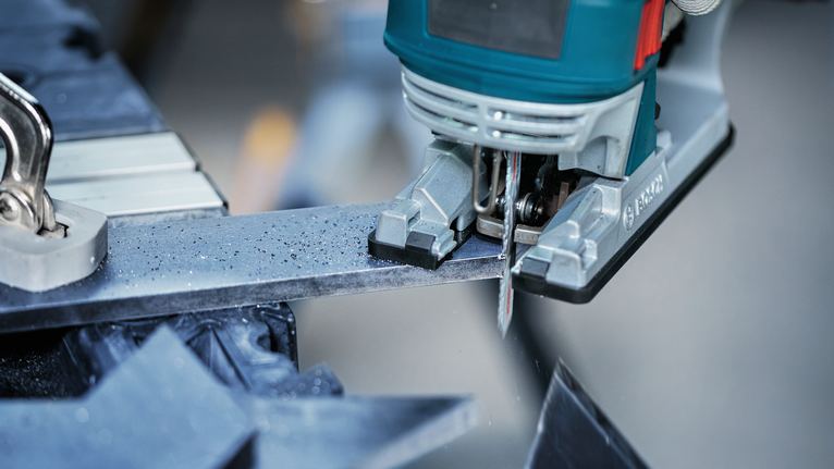 Stichsäge schneidet in einer Werkstatt durch eine Metallstange.