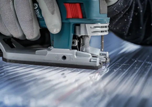 Eine Person mit Sicherheitsausrüstung schneidet ein Metallblech mit einer Stichsäge.