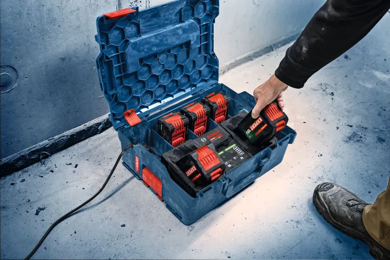 Eine Person legt eine Batterie in eine tragbare Ladestation auf dem Boden einer Werkstatt.