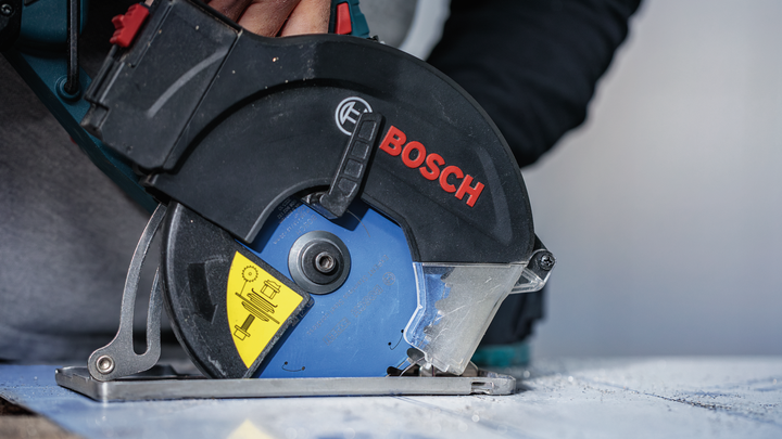 Eine Person mit Sicherheitsausrüstung schneidet mit einer Kreissäge eine Materialplatte.