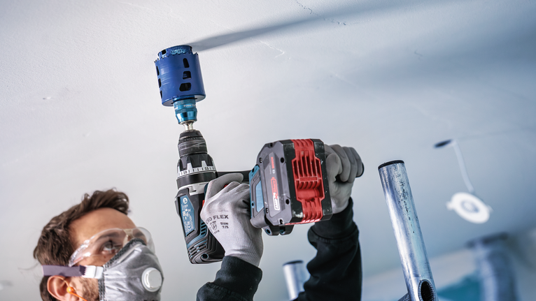 Eine Person mit Sicherheitsausrüstung bohrt mit einem Elektrowerkzeug ein großes Loch in eine Decke.