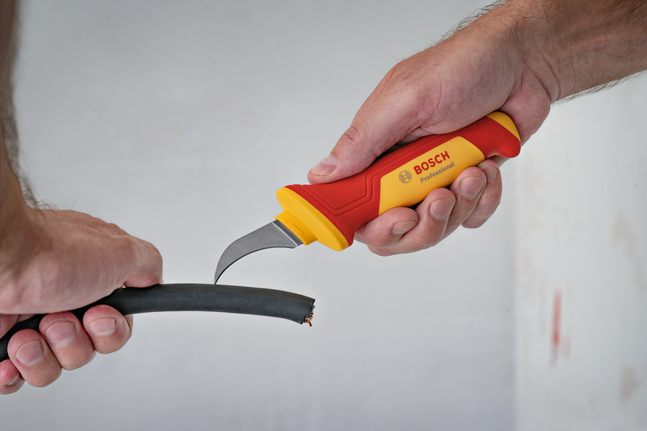 Eine Person entfernt mit einem isolierten Messer die äußere Schicht eines dicken Kabels.