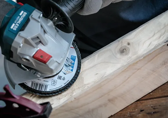 Person, die mit einem Winkelschleifer die Kante eines Holzbretts schleift.