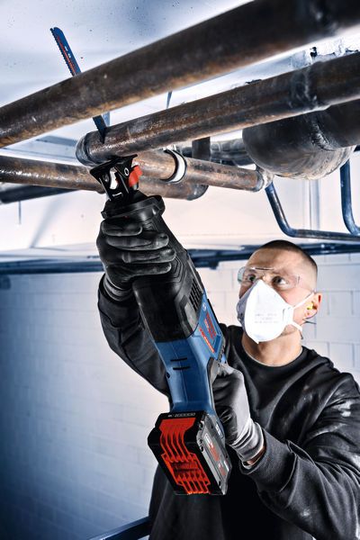 Eine Person mit Sicherheitsausrüstung verwendet eine kabellose Säbelsäge, um Metallrohre zu schneiden.