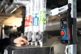 Eine Person inspiziert Rohre, während ein digitales Multimeter in der Nähe die Temperatur misst.