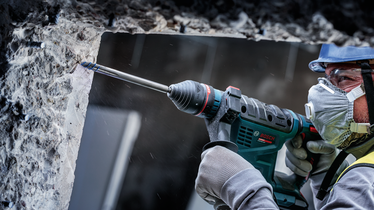Eine Person mit Schutzausrüstung bohrt mit einem Bohrhammer in eine Betonwand.
