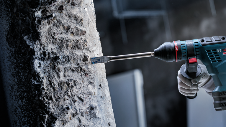 Eine Person mit Schutzausrüstung meißelt Beton mit einem Bohrhammer.