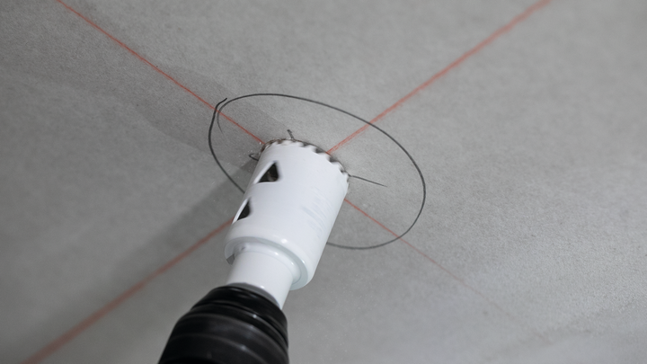 Mit einer Lochsäge wird ein kreisförmiger Schnitt in eine Decke gebohrt, der mit roten Führungslinien markiert ist.