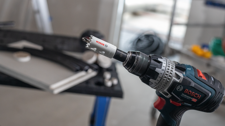 Akku-Bohrmaschine mit angebrachtem Lochsägenaufsatz, auf einer Werkbank liegend.