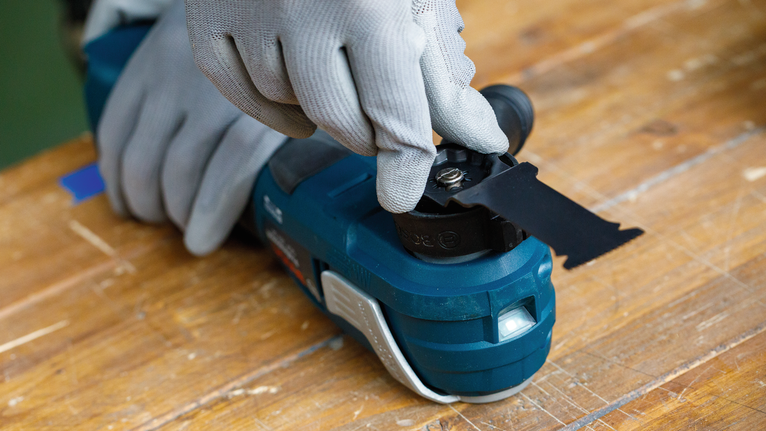 Eine Person mit Sicherheitsausrüstung befestigt eine schwarze Schneidklinge an einem Elektrowerkzeug.