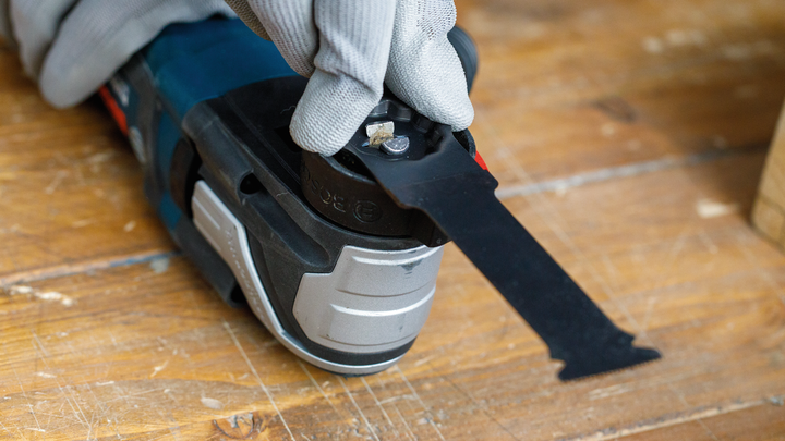 Eine Person mit Sicherheitsausrüstung installiert ein Sägeblatt an einem Elektrowerkzeug.